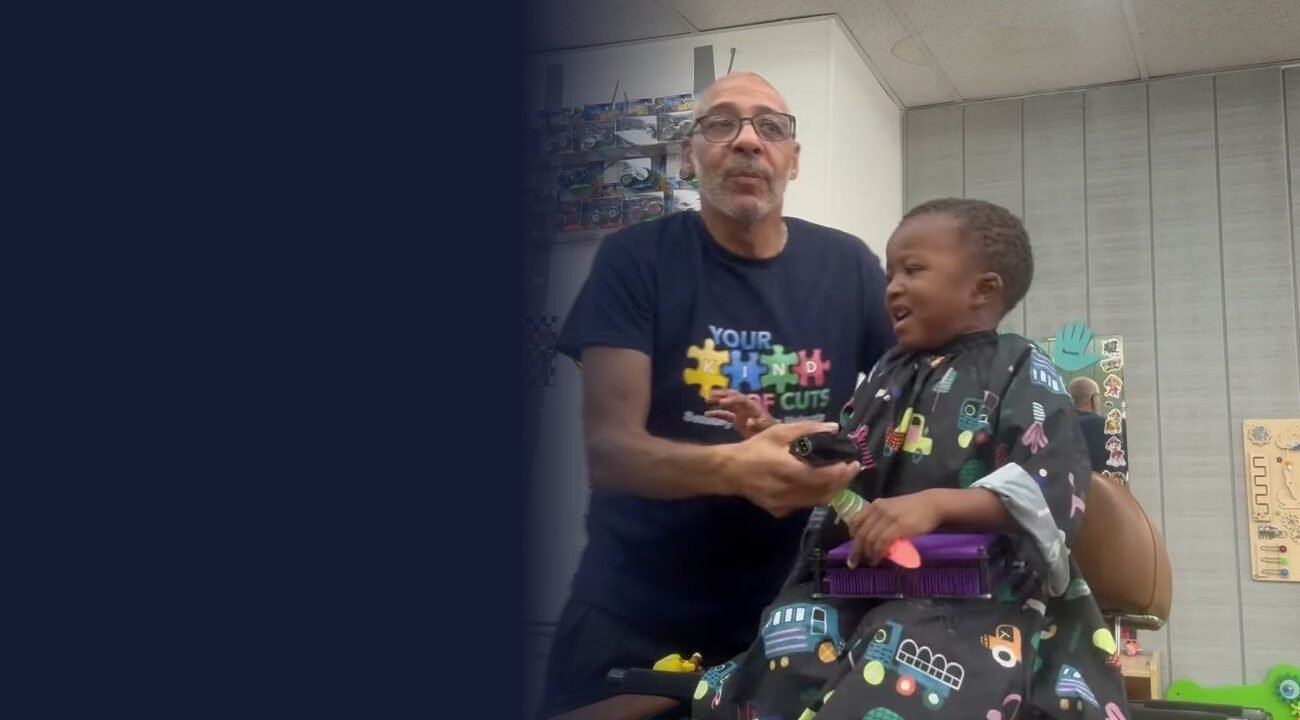 Smiling barber in a Your Kind of Cuts shirt giving a calm haircut to a happy young client